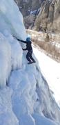 Derek approaching the top of his route. He's swinging his right tool high with excellent feet. His beanie is pulled down over his face underneath a bright blue helmet